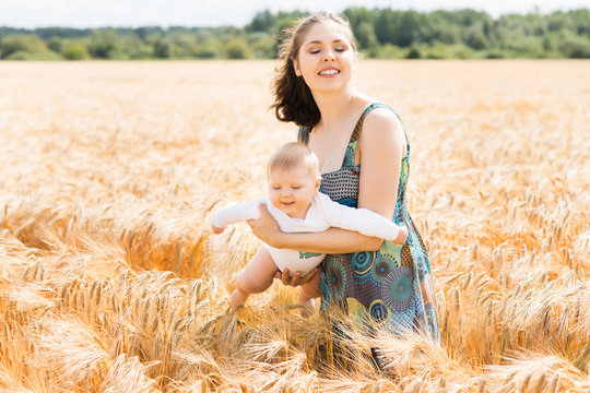 Young and beautiful woman playing with her infant baby in a meadow of wheat. Summer concept.