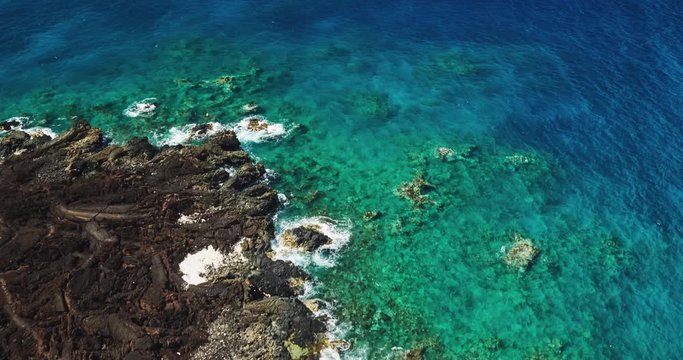 Aerial view over black lava flow and tropical blue ocean coral reef