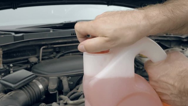 Man driver opens jerry can bottle with pink windshield washer fluid. Customers vehicle service and maintenance scene. 4K UHD video footage.