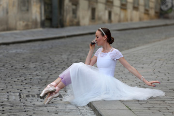 Fototapeta na wymiar Elegant ballerina sitting on the pavement and drinking a coffee