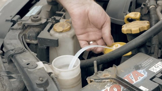 Driver or auto mechanic pours pink windshield washer fluid from jerry can bottle into the car. Customers vehicle service and maintenance scene. 4K UHD video footage.