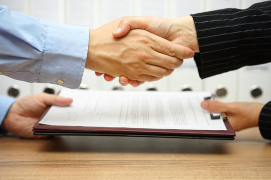 business partners are handshaking and exchanging contract after