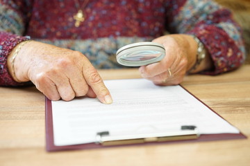 elderly person with magnifying glass checking document