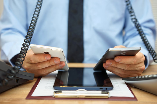 busy businessman in office at the desk using two mobile phones,