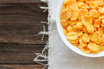Tasty corn flakes in bowl. Rustic wooden background with homespun napkin. Healthy crispy breakfast snack. Top view, flat lay.