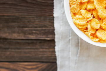 Tasty corn flakes in bowl. Rustic wooden background with homespun napkin. Healthy crispy breakfast snack. Top view, flat lay.