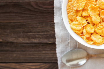 Tasty corn flakes in bowl. Rustic wooden background with homespun napkin. Healthy crispy breakfast snack. Place for text. Top view, flat lay.