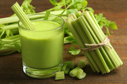 Fresh green celery juice in glass on wooden brown background