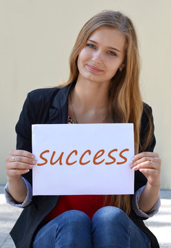 Cheerful,beautiful,light-haired,nice,with nice,cute smile girl,student sitting with inscription,success,concept,text,black words on the white paper,key,succeed,puzzle,blackboard,motivation,achievement