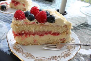 Piece of gateau with strawberry and vanilla cream inside, blueberry, raspberry and cream on top
