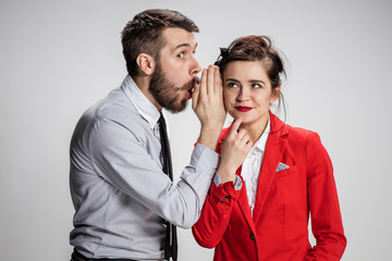 Young man telling gossips to his woman colleague at the office