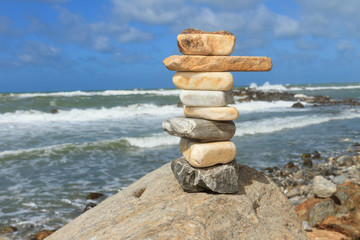 Vertical rock balancing over a cliff on a shore near the rough sea