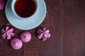 French pink meringue cookies and cup of tea on wooden background