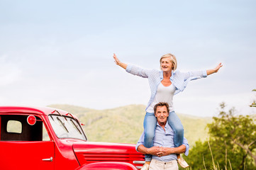 Senior couple standing at the red vintage car