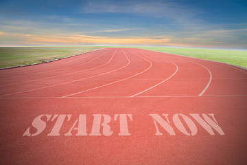 Start now written on Running track with green grass and blue sky