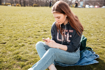 Obraz premium Woman listening to music from smartphone sitting on grass
