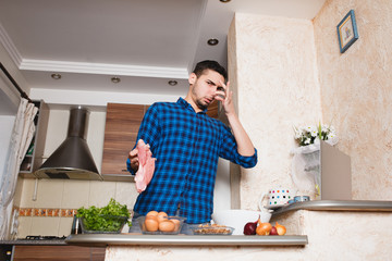 young man preparing meat in her kitchen , looking into the card , the meat in his hand