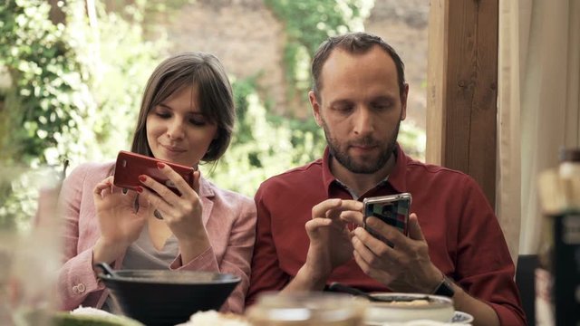 Young couple using smartphones sitting in cafe in garden

