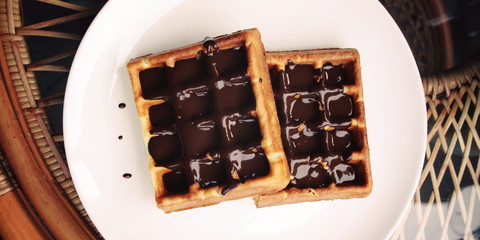 Vienna Waffles with chocolate topping. Aged. Delicious dessert. White plate with Chocolate covered Wafers. Toned. Delicious dessert. Wide photo for wallpaper or site slider. Unhealthy but delicious.