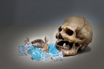 decayed teeth human skull with candy on wood background. like a people eating candy too much.