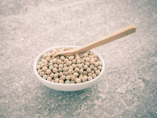 White pepper corns in bowl with wooden spoon.The white peppercorns are a nice  ingredient for cooking with hot spice. Dried seasoning for spicy food on stone kitchen table.