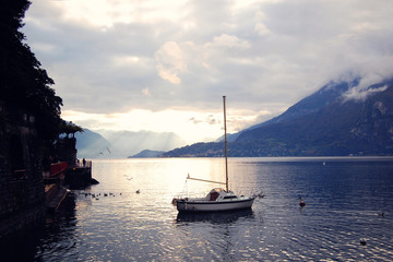 Fototapeta premium Boat on Lake Como at the sunset. Silver linings in Lake Como at the sunset. Retro style photo. Sunset view of the lake in Lombardy. Varenna, Lake Como, Italy.