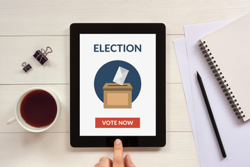 Online voting concept on tablet screen with office objects on white wooden table. All screen...