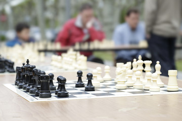 In the foreground a chessboard, in the background (out of focus) several players in a chess simultaneous exhibition