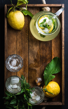 Homemade mint lemonade served with fresh lemons and ice over wooden background, top view, copy space