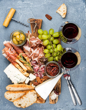 Cheese and meat appetizer selection or wine snack set. Variety of cheese, salami, prosciutto, bread sticks, baguette, honey, grapes, olives, sun-dried tomatoes, pecan nuts over grey concrete textured