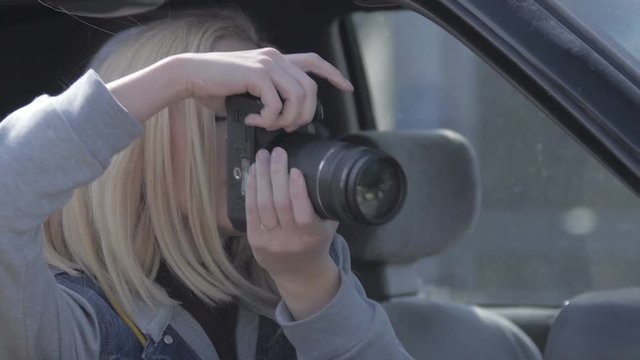 Blond girl taking photos from window with professional camera in old dodge car