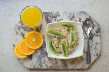 Fototapeta na wymiar Bowl of oatmeal porridge with kiwi on marble table