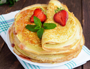 Pile of golden pancakes with strawberries and strawberry jam, decorative sprig of mint. Close-up
