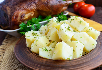 Boiled potatoes in a clay bowl close-up and roasted goose