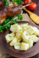 Boiled potatoes in a clay bowl close-up and roasted goose