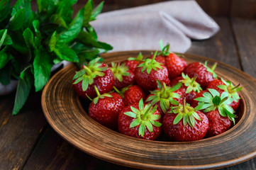 Ripe strawberries in a clay bowl, and mint leaves. close-up on wooden background.