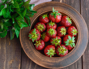 Ripe strawberries in a clay bowl, and mint leaves. On wooden background. The top view