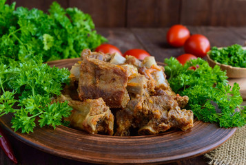 Pork ribs steamed with carrots, parsley decorated in a clay bowl on a wooden background. Close up