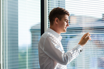 business man in a suit with cufflinks looking out of window through the blinds. waiting concept....