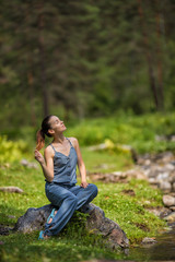 Young girl in a denim dress sits on a stone in a forest