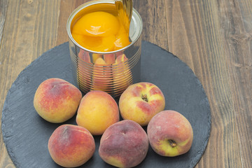 lata con melocotones en conserva, melocotones frescos alrededor de la lata
