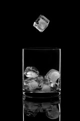 Ice cube falling into a glass on a black background