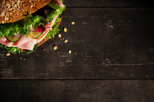 Sandwich with vegetables, ham and cheese on dark wood background, top view
