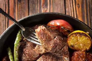 Piece of grilled beef steak on fork with vegetables with vegetables in the pan