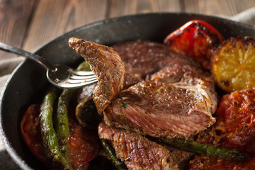 Piece of grilled beef steak on fork with vegetables with vegetables in the pan