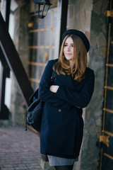 Beautiful young woman wearing hat and dark-blue coat walking on a city street