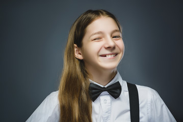 Portrait of cute girl winking over gray background. Looking at the camera. Positive human emotion facial expression body language