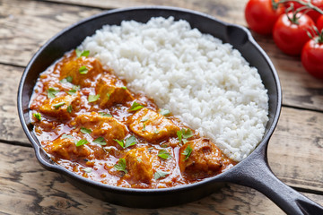 Tikka masala traditional Indian butter chicken spicy meat food and rice with tomatoes in cast iron skillet on vintage wooden background. Karahi chicken recipe