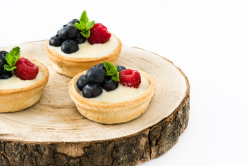 Delicious tartlets with raspberries and blueberries on tree trunk isolated
