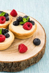 Delicious tartlets with raspberries and blueberries on tree trunk
